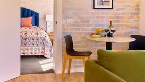 A room with a bed, a round table with chairs, a brick wall, and a framed picture on the wall.