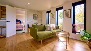 Una habitación con un sofá verde, una mesita de mimbre y vistas amplias a través de grandes ventanales.