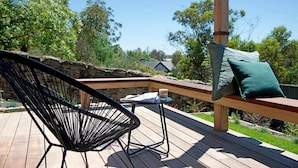 Una terraza de madera con una silla negra, una mesa pequeña y un banco con un cojín.