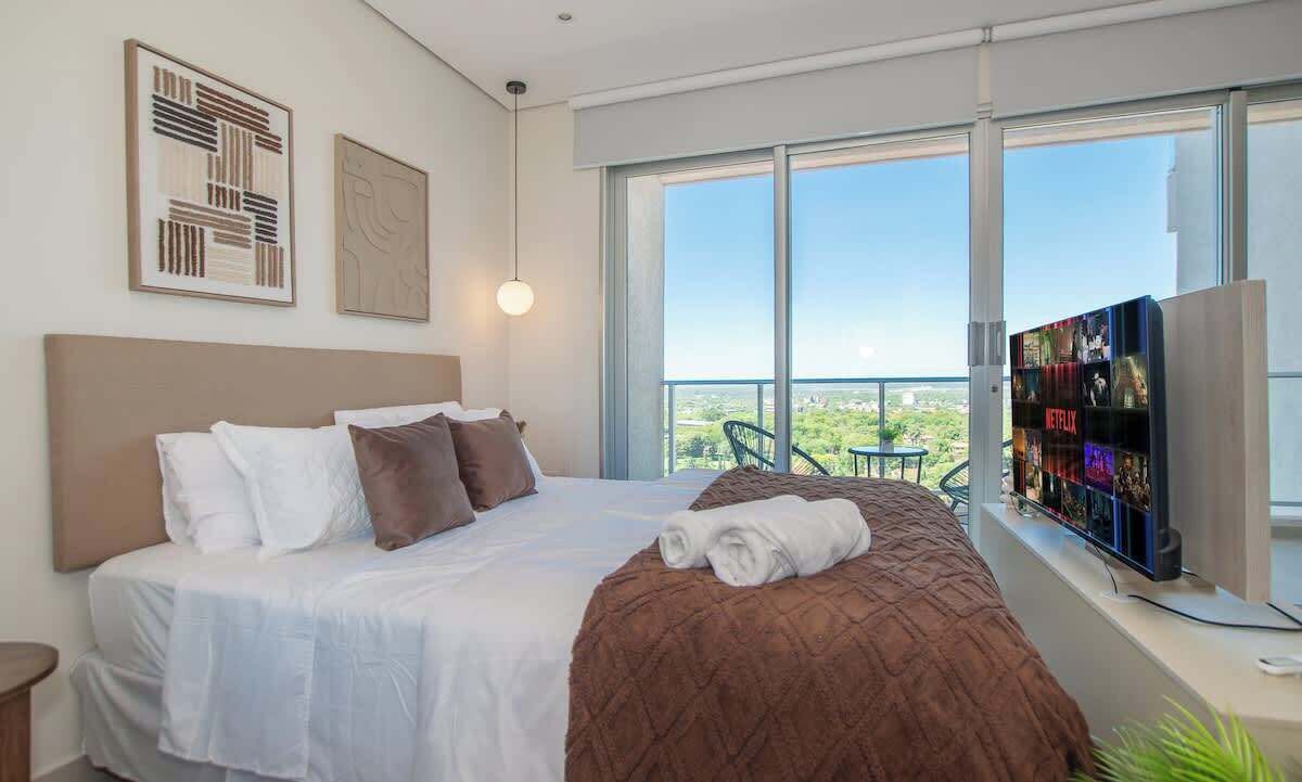 A modern hotel room with a large bed, a TV, and a balcony with a view.