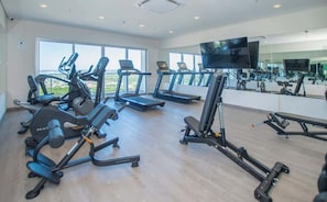 Ein Fitnessstudio mit Laufbändern, Kraftgeräten und einem Fernsehbildschirm.