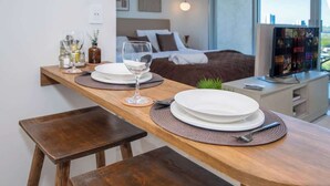 Ein ordentlich eingerichteter Essbereich mit einem Holztisch, zwei Hocker und einem Bett im Hintergrund.