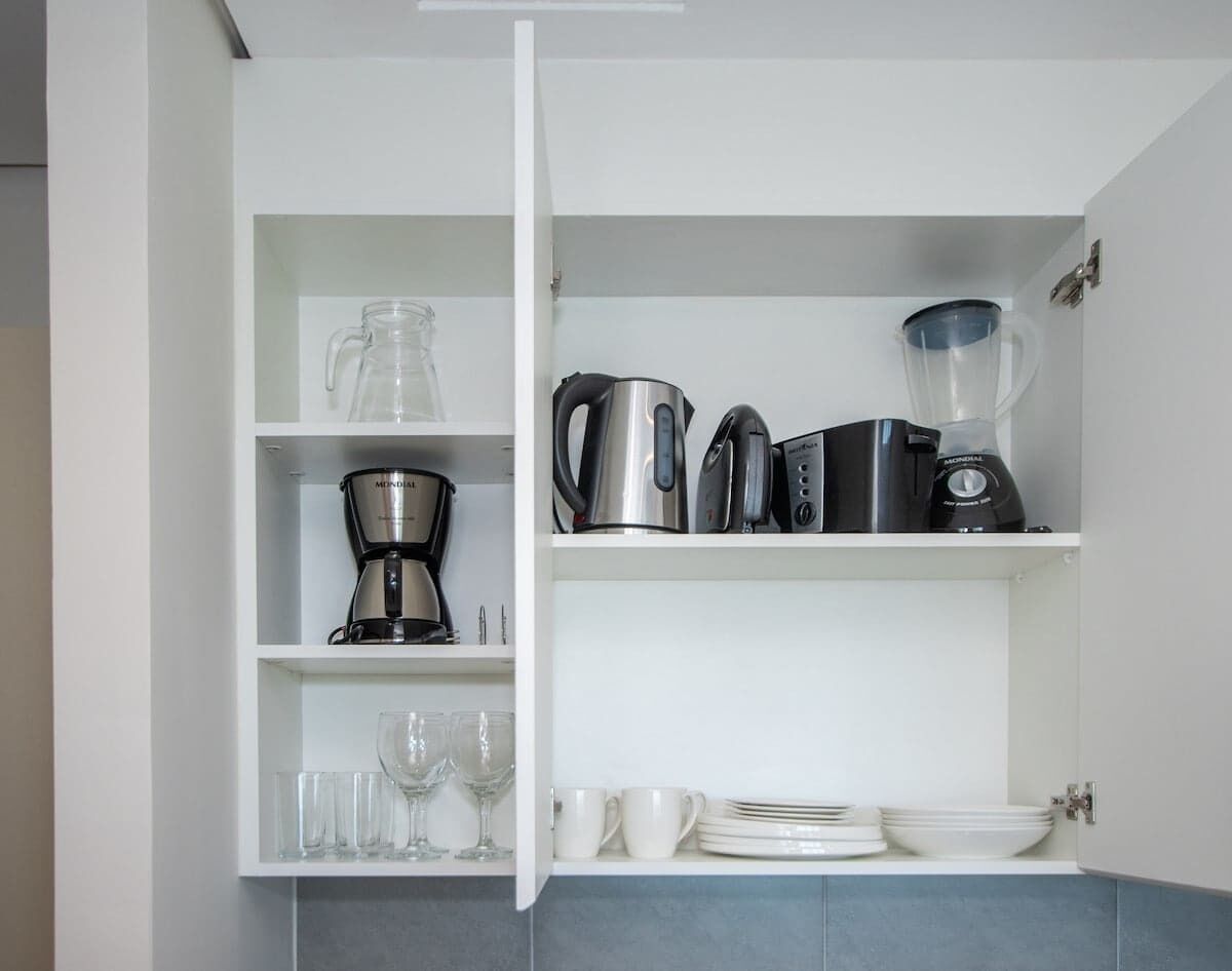 Una cocina con cafetera, hervidor, licuadora y cristalería en estantes.