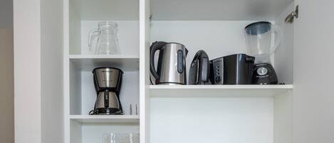 Una cocina con cafetera, hervidor, licuadora y cristalería en estantes.