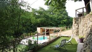 A backyard with a swimming pool, a wooden deck, and a stone wall.