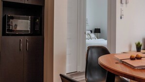 Una camera d'albergo moderna con un armadietto in legno scuro, un forno a microonde, un tavolo da pranzo con sedie e vista sulla stanza comunicante.