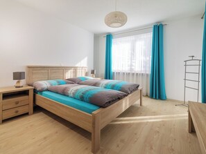 A bedroom with a wooden bed, a nightstand, a lamp, a floor lamp, and a window with curtains. - Alpen Leukerbad # 4-bed apartment, Dusche, WC by Interhome (Leukerbad)