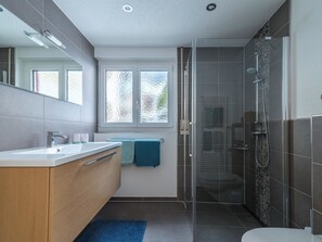 Un bagno moderno con cabina doccia in vetro, mobile lavabo in legno e uno specchio grande.