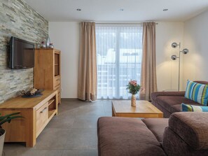A modern living room with a television, wooden furniture, a sofa, a coffee table, and a window with curtains. - Alpen Leukerbad # 4-bed apartment, Dusche, WC by Interhome (Leukerbad)