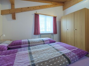 A bedroom with a bed, a window with curtains, a radiator, and wooden wardrobe. - Alpen Leukerbad # 4-bed apartment, Dusche, WC by Interhome (Leukerbad)