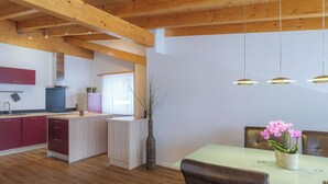 Una cocina moderna con vigas de madera, un comedor con mesa y sillas, y un florero con flores.