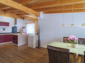 Eine moderne Küche mit Holzbalken, einem Essbereich mit Tisch und Stühlen sowie einer Vase mit Blumen.