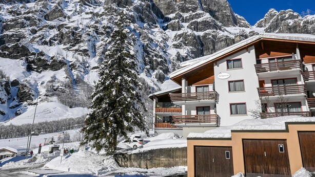 Una montaña nevada con un edificio que tiene balcones y un letrero 'Alpen'.