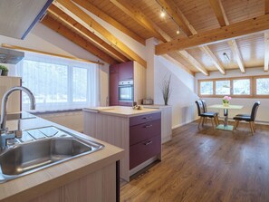 A modern kitchen with wooden beams, a large island, and a dining area with a table and chairs. - Alpen Leukerbad # 4-bed apartment, Dusche, WC by Interhome (Leukerbad)