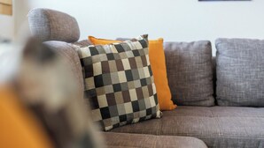 Un sofá modular con varios cojines, incluyendo uno de cuadros y uno naranja liso.