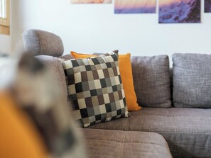 Ein modulares Sofa mit mehreren Kissen, darunter eines kariert und eines einfarbig orange.