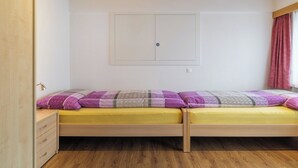 Una habitación con techo de madera, una cama con colchón amarillo y ropa de cama morada, un armario de madera y una ventana con cortina roja.