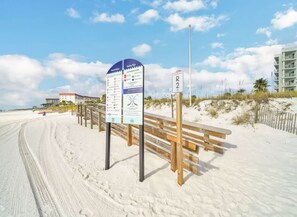 En strand med en träbänk och en informationsskylt med säkerhetsanvisningar.