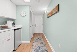 A narrow hallway with a kitchen area on the left, a clock on the wall, and a 'hello' sign on the right. - 3/3 Ocean front/views, heated pool 2 king bed (Fort Walton Beach)