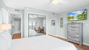 Un dormitorio con cama, ventilador de techo, televisor y vistas al exterior.