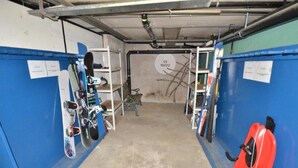 A garage with blue walls, a concrete floor, and various items including a red object, a bench, and shelves with items. - Fortuna 302 # 3-bed apartment, Dusche, WC 3-Bettwohnung, Dusche, WC by Interhome (Leukerbad)