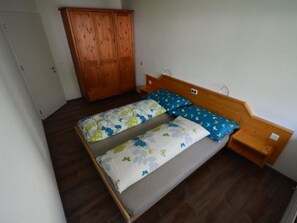 A room with a wooden bed, a wardrobe, and a small wooden nightstand. - Fortuna 302 # 3-bed apartment, Dusche, WC 3-Bettwohnung, Dusche, WC by Interhome (Leukerbad)