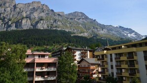 A mountain town with buildings in the foreground and a large mountain in the background. - Fortuna 302 # 3-bed apartment, Dusche, WC 3-Bettwohnung, Dusche, WC by Interhome (Leukerbad)