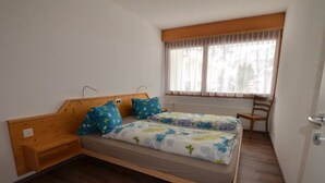 A single bed with a wooden headboard, a window with sheer curtains, and a wooden chair. - Fortuna 302 # 3-bed apartment, Dusche, WC 3-Bettwohnung, Dusche, WC by Interhome (Leukerbad)