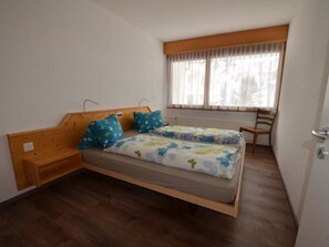 A single bed with a wooden headboard, a window with sheer curtains, and a wooden chair. - Fortuna 302 # 3-bed apartment, Dusche, WC 3-Bettwohnung, Dusche, WC by Interhome (Leukerbad)