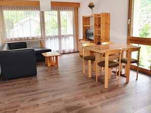 Ein Wohnzimmer mit einer Couch, einem Holztisch, Stühlen, einem Fernseher und einem Bücherregal.