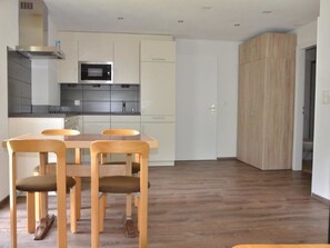 A modern kitchen with white cabinets, a microwave, and a dining area with wooden chairs and a table. - Fortuna 302 # 3-bed apartment, Dusche, WC 3-Bettwohnung, Dusche, WC by Interhome (Leukerbad)