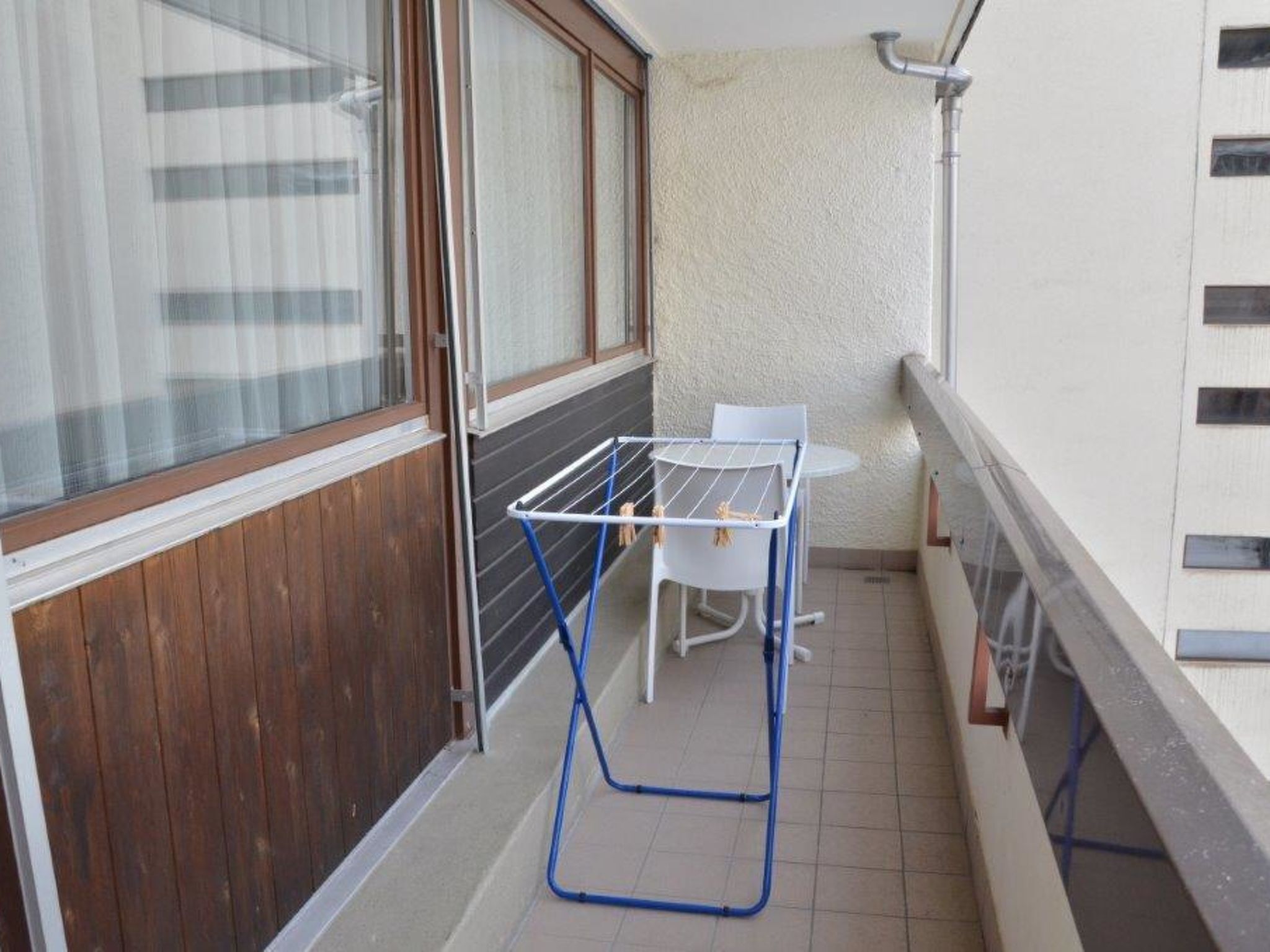 A balcony with a drying rack, a chair, and a window with curtains.