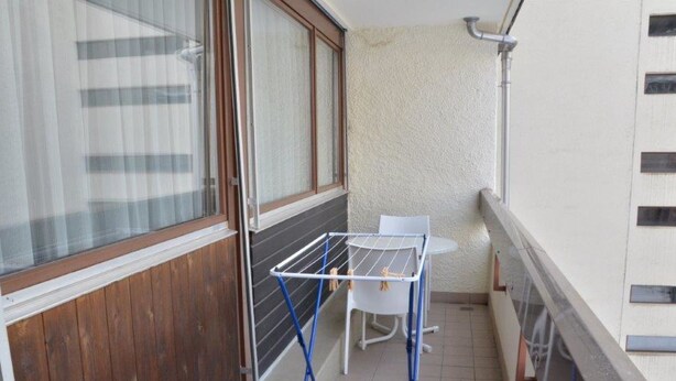 A balcony with a drying rack, a chair, and a window with curtains. - Fortuna 302 # 3-bed apartment, Dusche, WC 3-Bettwohnung, Dusche, WC by Interhome (Leukerbad)