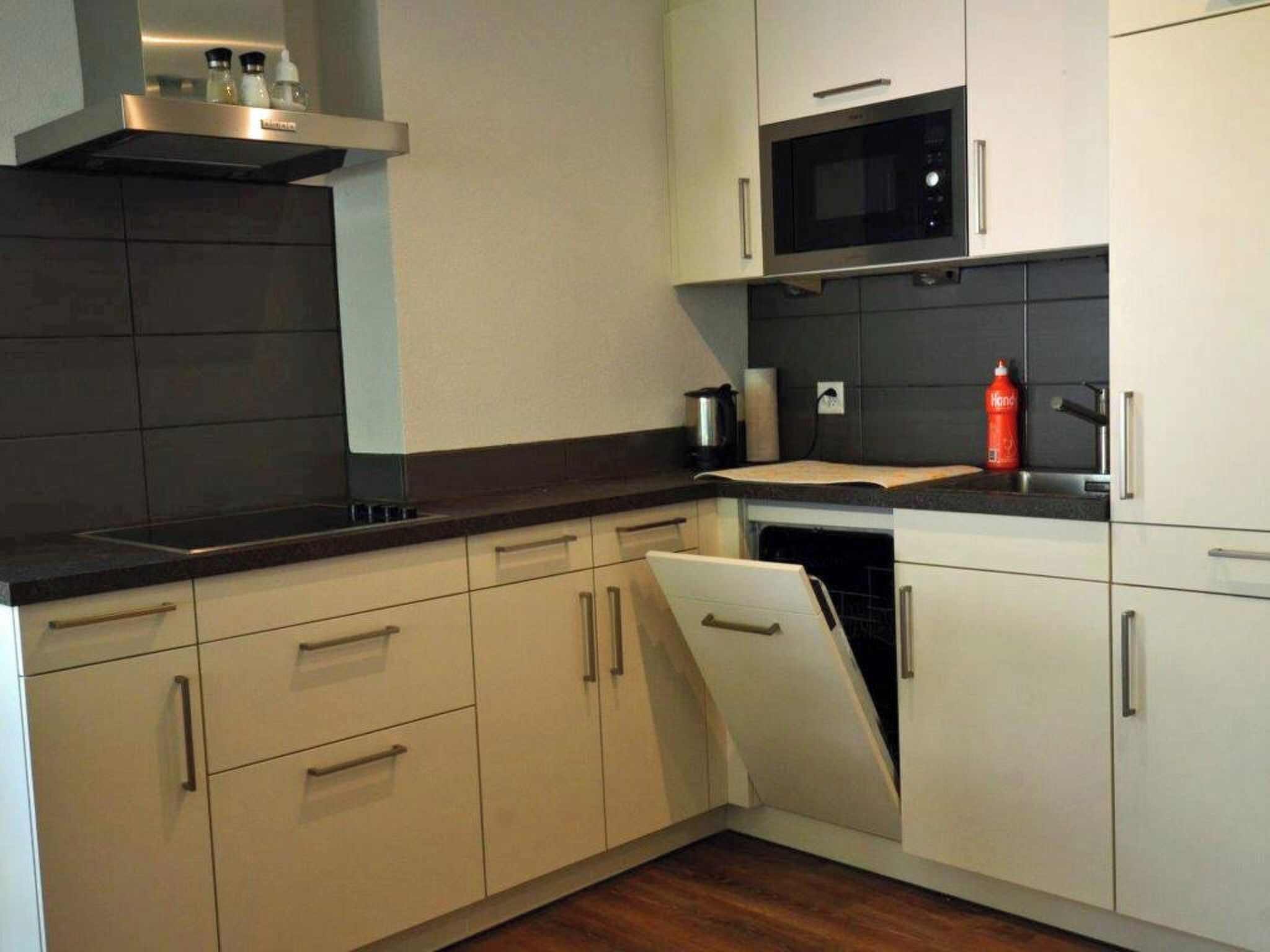 A modern kitchen with white cabinetry, a black countertop, a microwave, and a dishwasher.