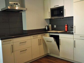 A modern kitchen with white cabinetry, a black countertop, a microwave, and a dishwasher. - Fortuna 302 # 3-bed apartment, Dusche, WC 3-Bettwohnung, Dusche, WC by Interhome (Leukerbad)
