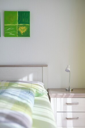 A bedroom with a bed, a bedside table with a lamp, and a green artwork on the wall. - Alpen Leukerbad # 4-bed apartment, Dusche, WC by Interhome (Leukerbad)