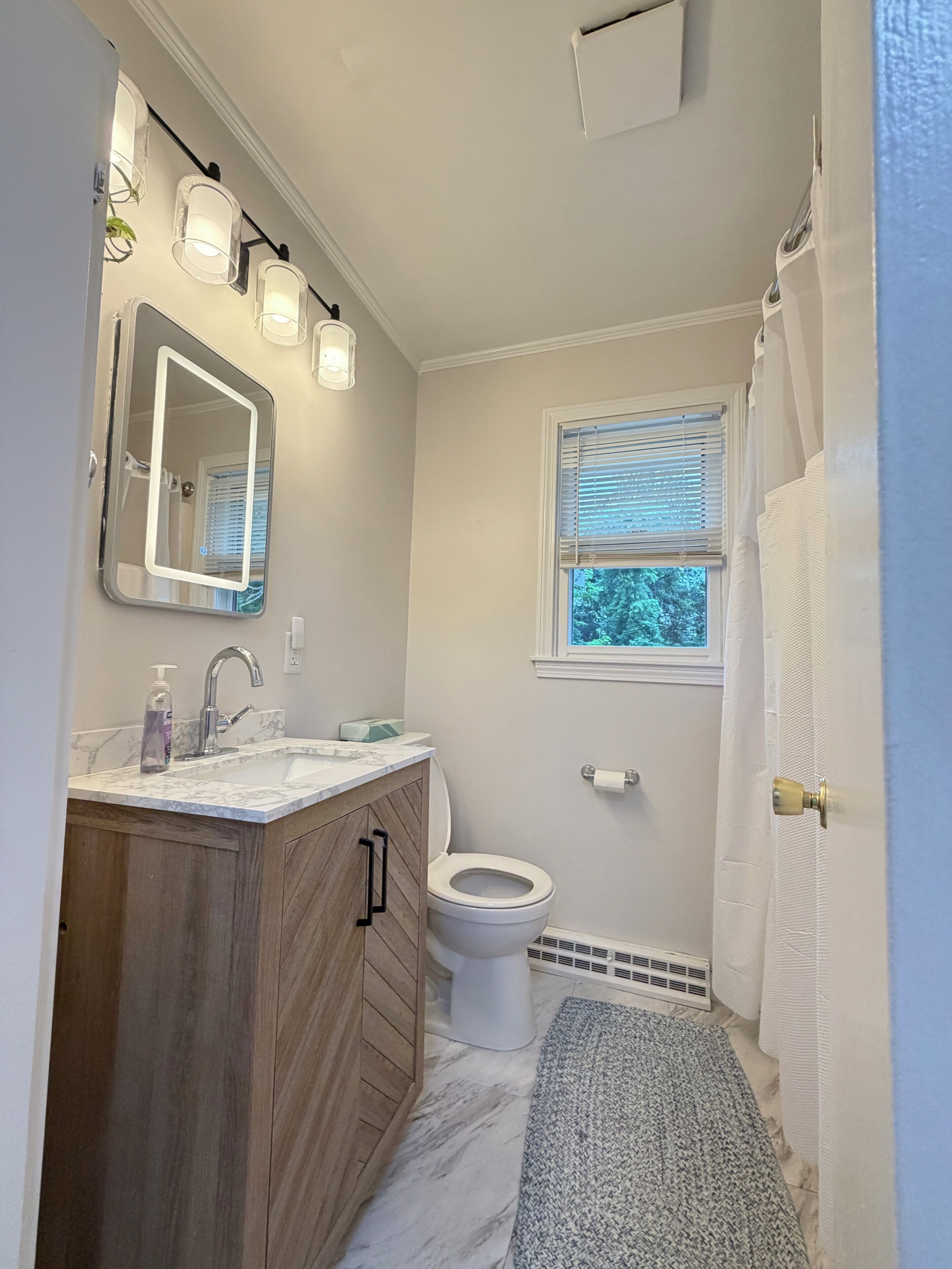 A bathroom with a vanity, sink, mirror, toilet, window, and shower curtain.