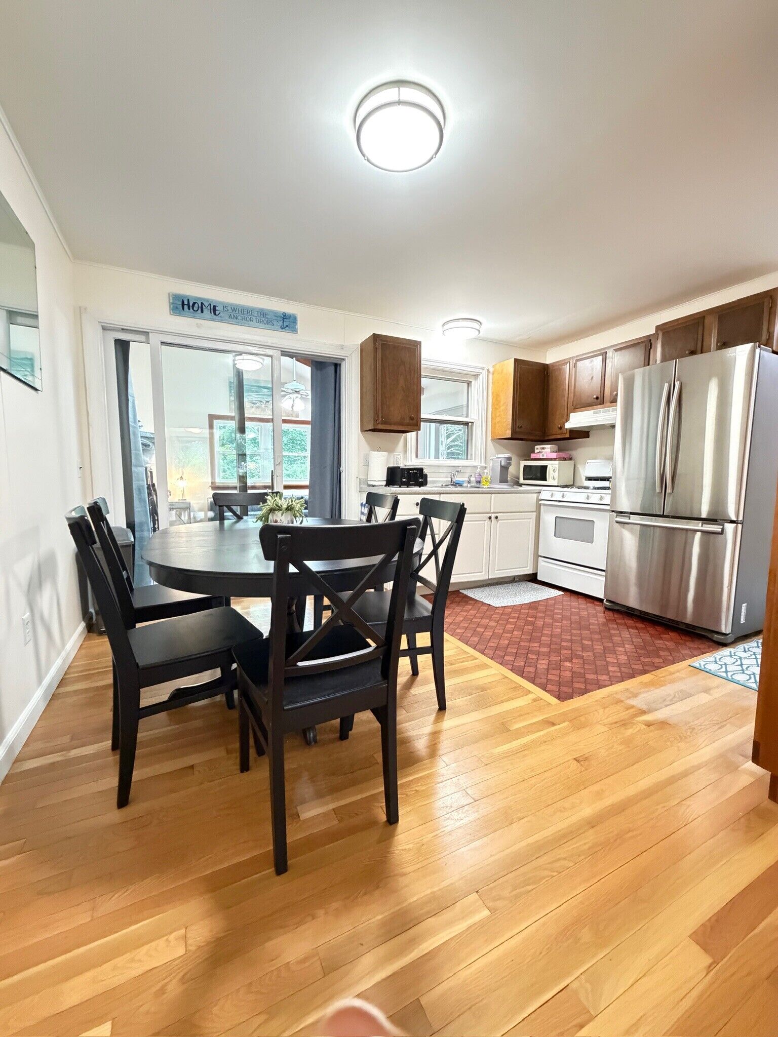 A modern kitchen with wooden cabinets, a stainless steel refrigerator, and a dining area with a round table and chairs.