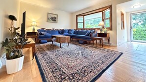 A living room with a blue sofa set, a wooden coffee table, a patterned rug, a TV, and a large window. - 2Bed 1Bath- ½ Mile walk to Mayflower, central A/C, CLEAN w/ washer/dryer (Dennis)