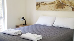A neatly made bed with pillows and folded towels, a bedside lamp, and a beach-themed wall art.