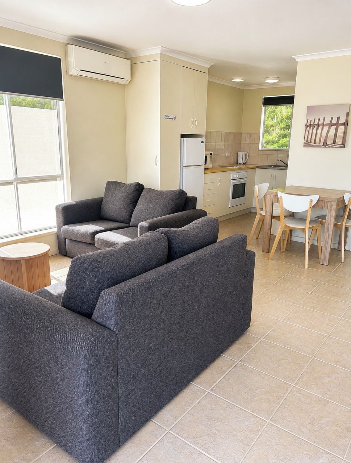 A modern living room with a grey sectional sofa, a small round table, and a dining area with a wooden table and chairs.