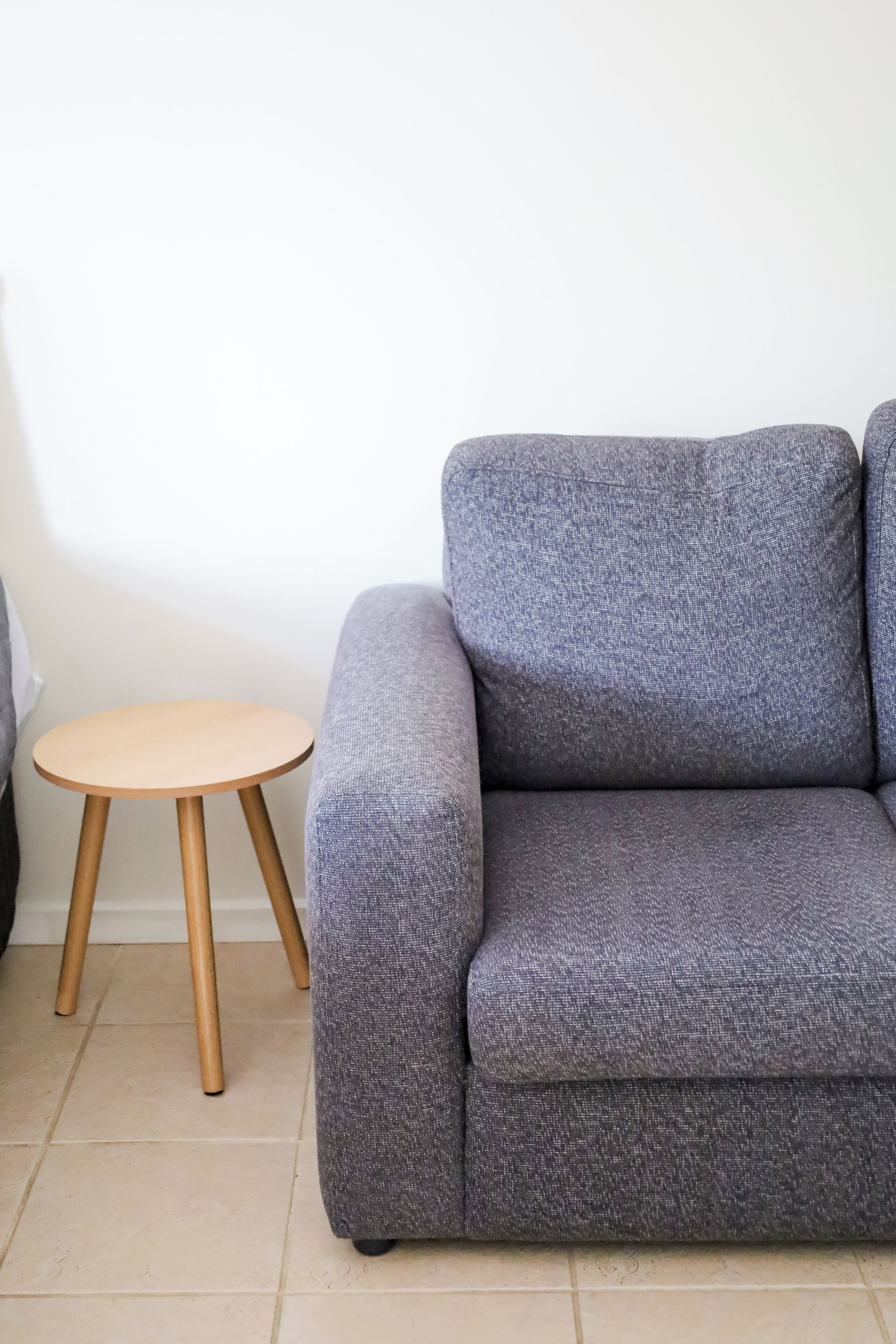 Un sofá gris con patas de madera y una pequeña mesa redonda de madera a un lado.
