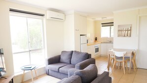 A modern living room with a grey sofa, a small table, and a kitchen area with a dining table and chairs.