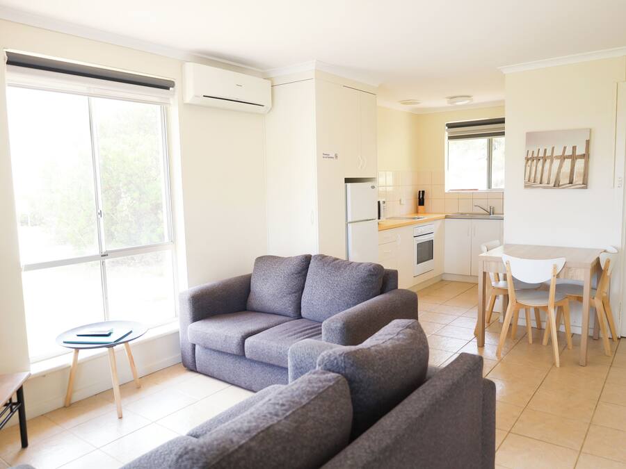 Un salon moderne avec un canapé gris, une petite table et un coin cuisine comprenant une table à manger et des chaises.