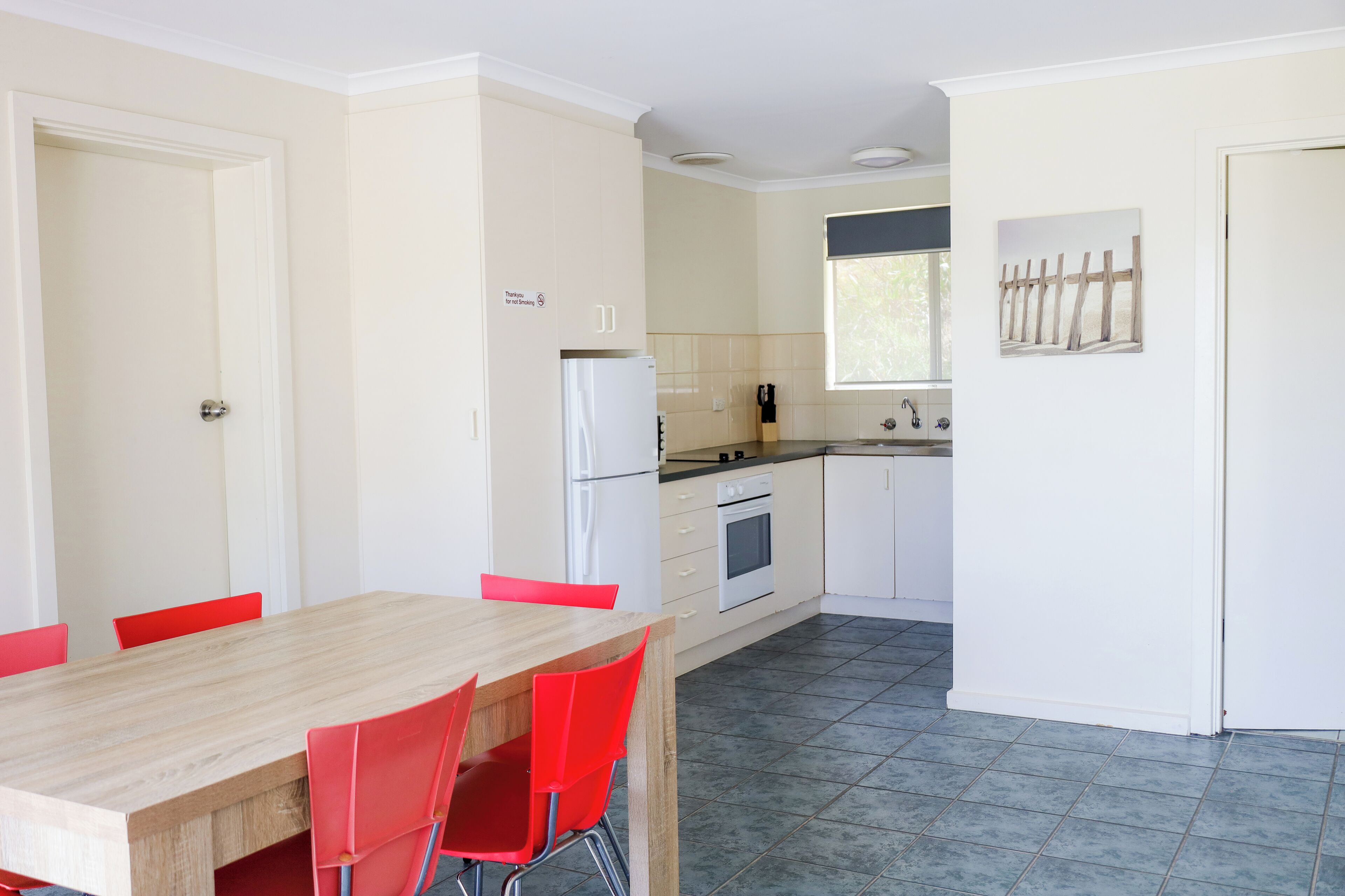 A compact kitchen with white cabinets, a refrigerator, and a dining area with a wooden table and red chairs.