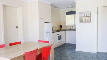 Cocina compacta con armarios blancos, un refrigerador y un comedor con mesa de madera y sillas rojas.