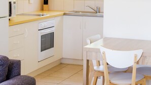 A compact kitchen with a microwave, oven, sink, and a dining area with chairs and a table.