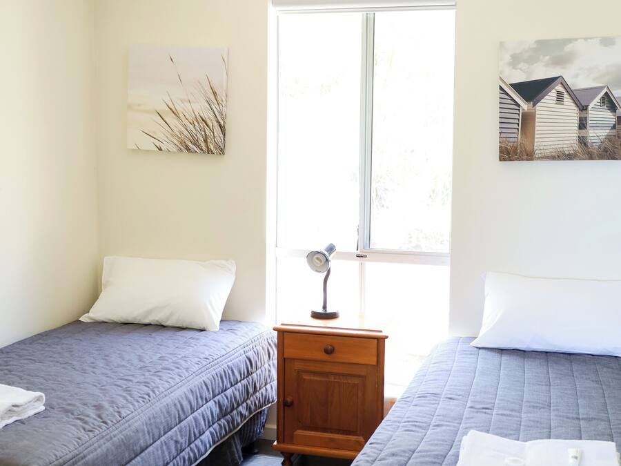 Ein Zimmer mit zwei Betten, einem Fenster, einem Nachttisch und Wandbildern.