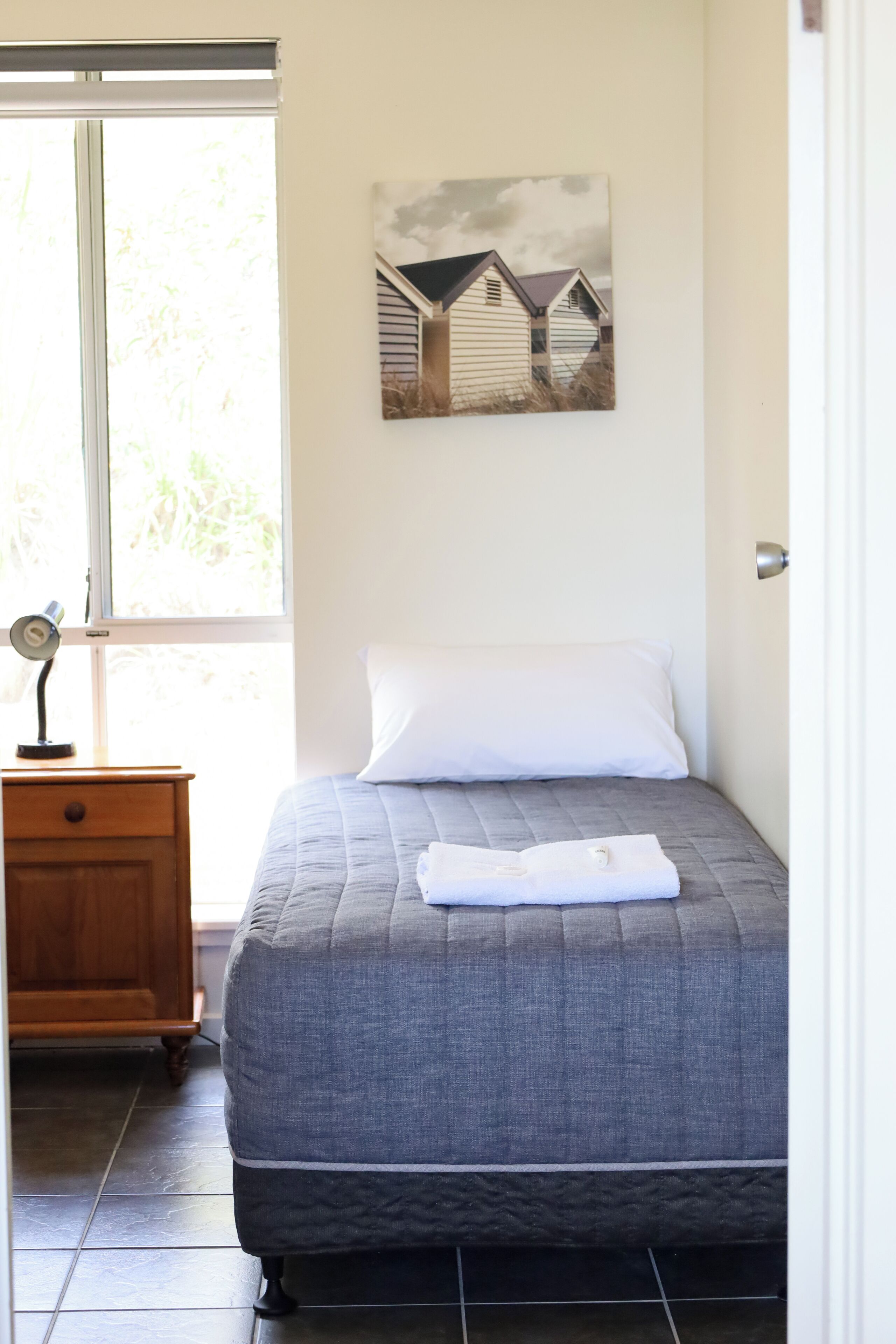 Un dormitorio con una cama, una mesita de noche, un cuadro en la pared y una ventana.