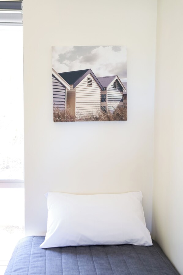 A bedroom with a bed, a pillow, and a wall-mounted picture of beach huts.